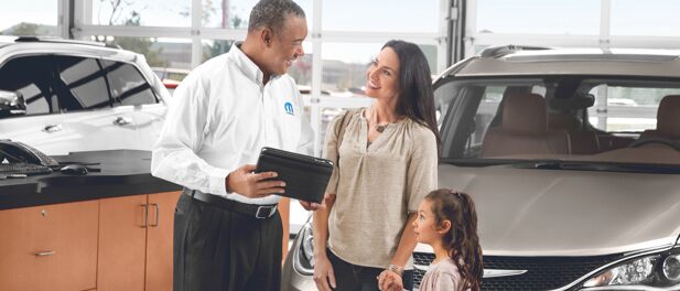 Mopar agent in dealership showroom checks FCA recall information for a mother with her child