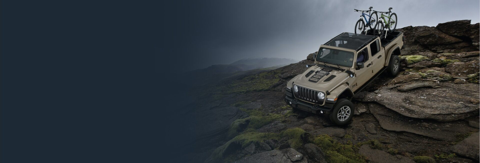 The 2022 Jeep Gladiator descending a rocky slope with two bicycles mounted on a carrier in the truck bed.